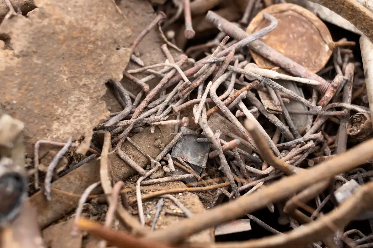Close-up of dirty, rusty scrap metal with bent nails, wire and flat steel pieces mixed together with dirt