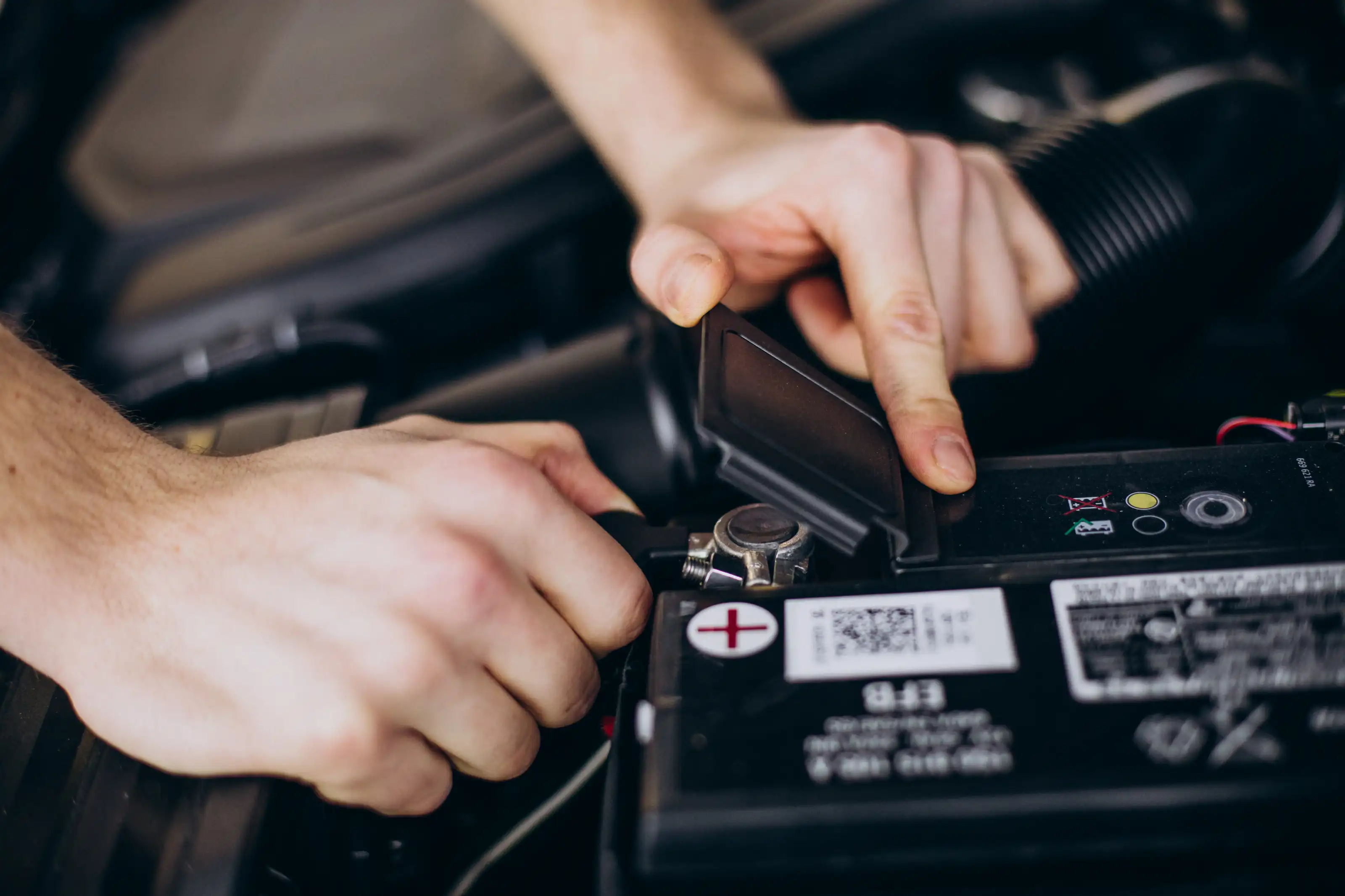 Close-up of a person's hands lifting the terminal cover on a car battery under the bonnet